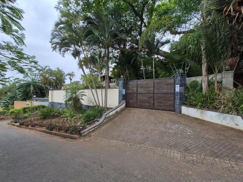 Front entrance view featuring a secure wooden driveway gate, perimeter wall with electric fencing, and established garden landscaping.