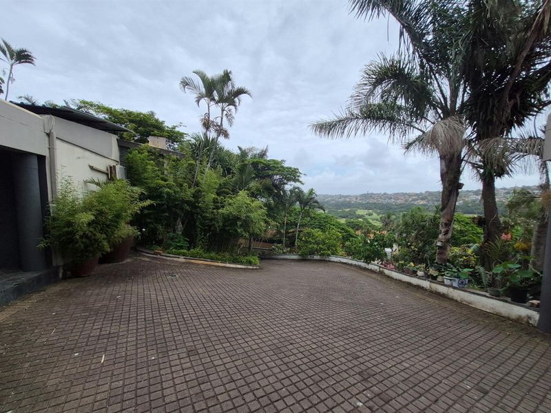 A paved driveway area leading to the property entrance, featuring established garden landscaping and scenic views of the surrounding neighborhood.