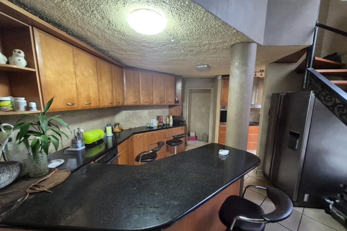 A functional kitchen featuring dark granite countertops, wooden cabinetry, a breakfast bar, and a central structural pillar, with an adjacent scullery area.