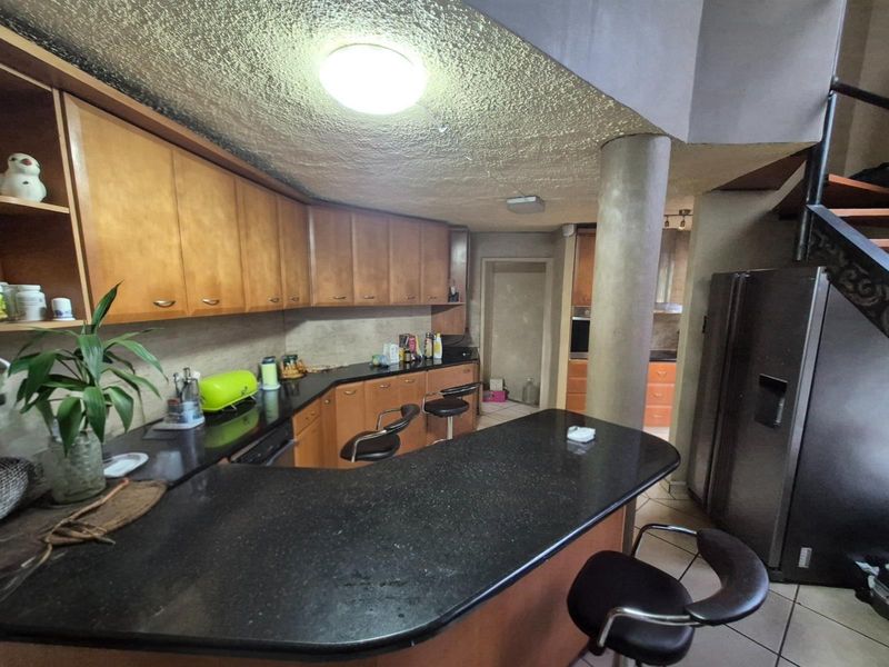 A functional kitchen featuring dark granite countertops, wooden cabinetry, a breakfast bar, and a central structural pillar, with an adjacent scullery area.