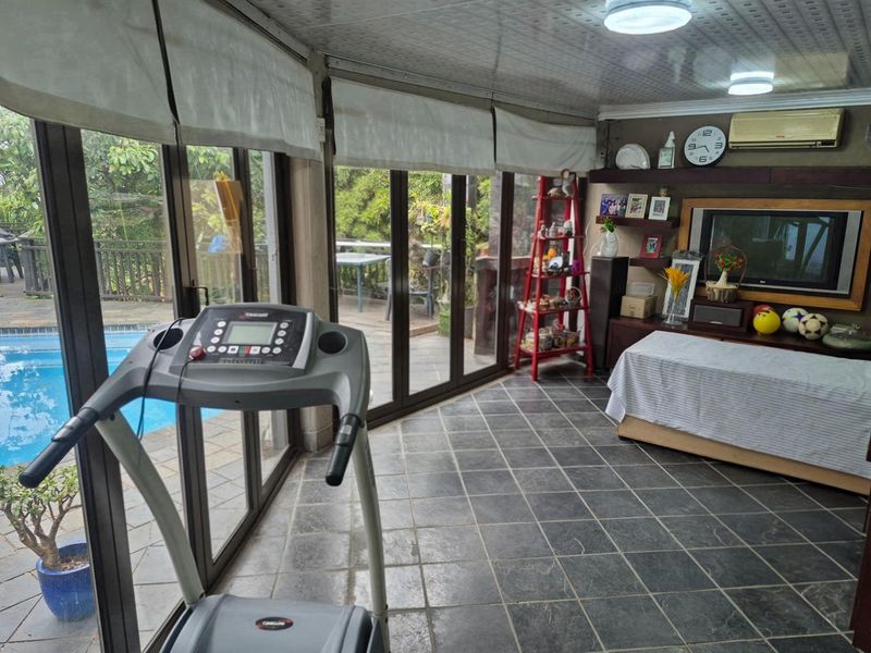 A versatile sunroom or enclosed patio featuring large glass sliding doors, tiled flooring, and direct access to the outdoor pool area.