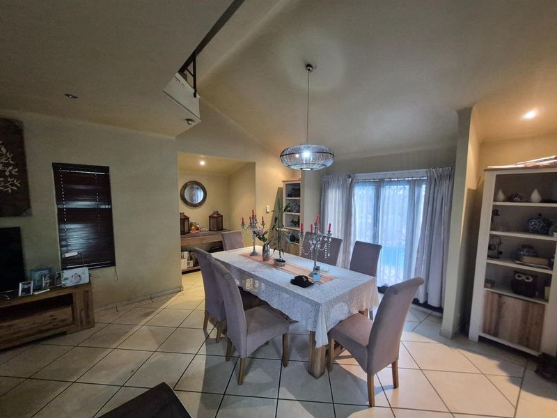 A spacious dining area featuring tiled flooring, a vaulted ceiling, and sliding glass doors providing access to the outdoor patio area.