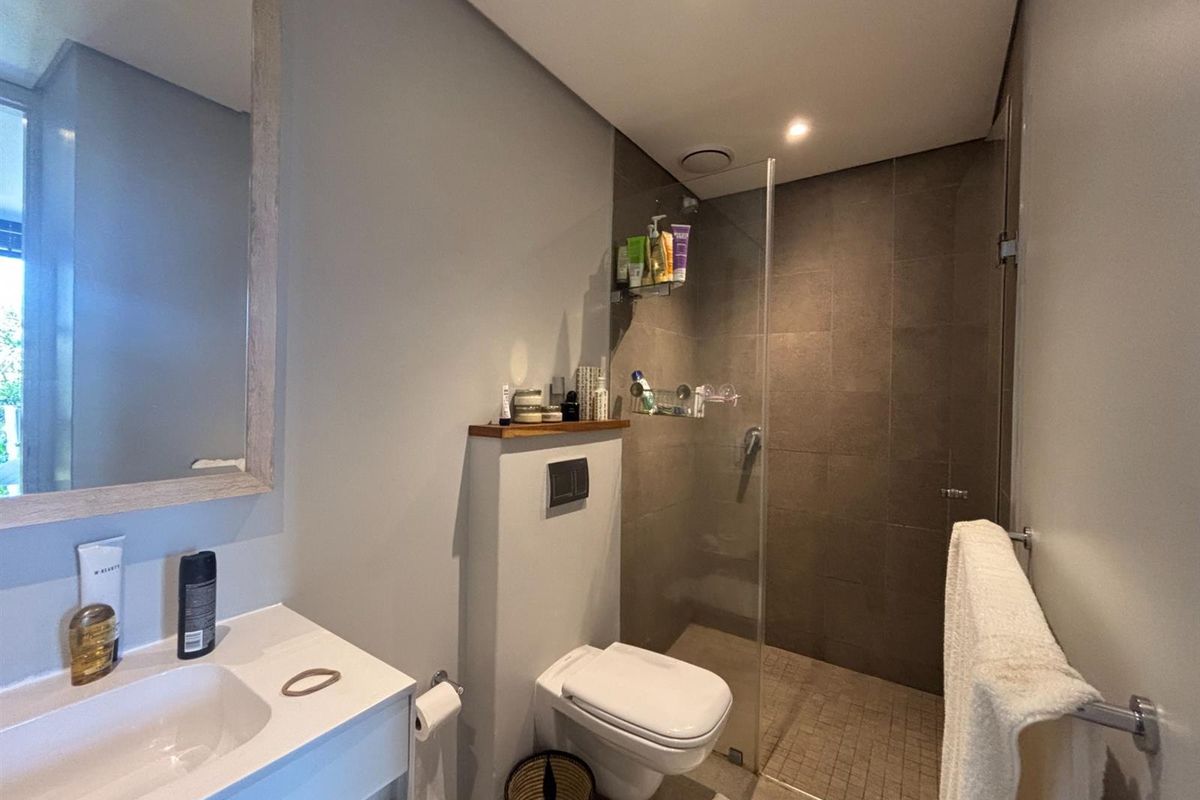 Modern bathroom featuring a walk-in shower with glass enclosure, wall-mounted toilet, and a vanity with integrated basin and mirror.