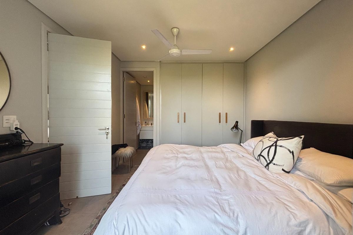 A well-maintained bedroom featuring built-in floor-to-ceiling wardrobes, a ceiling fan, and an en-suite bathroom entrance.