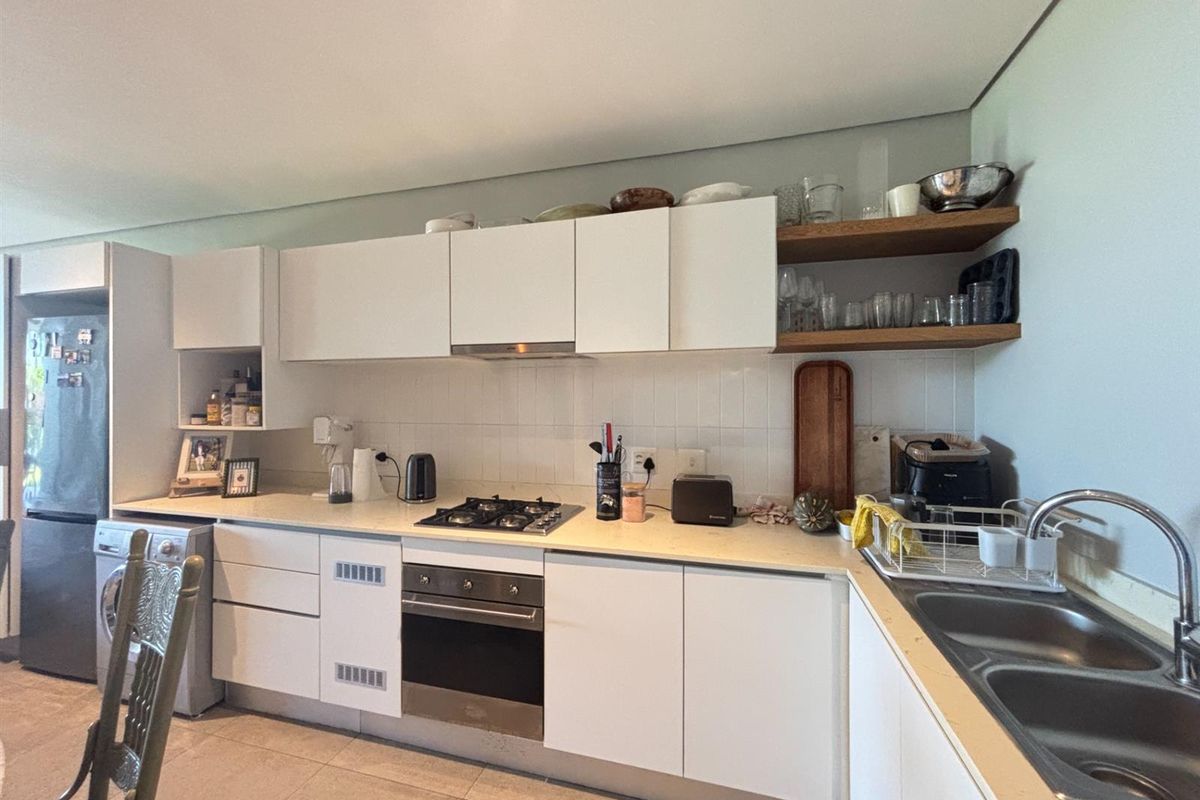A functional kitchen featuring white cabinetry, a built-in oven, gas hob, extractor fan, and a double stainless steel sink with tiled splashbacks.