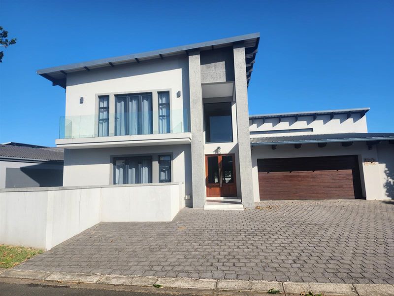 Modern double-storey residential facade featuring a paved driveway, integrated double garage, and a glass-balustrade balcony.