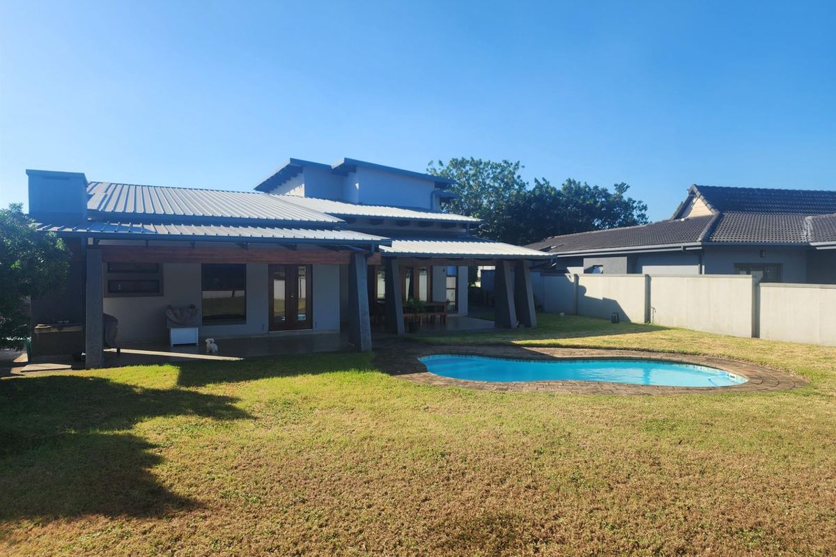 Rear view of the property featuring a covered patio area, a swimming pool with paved surround, and a well-maintained garden with boundary walls.