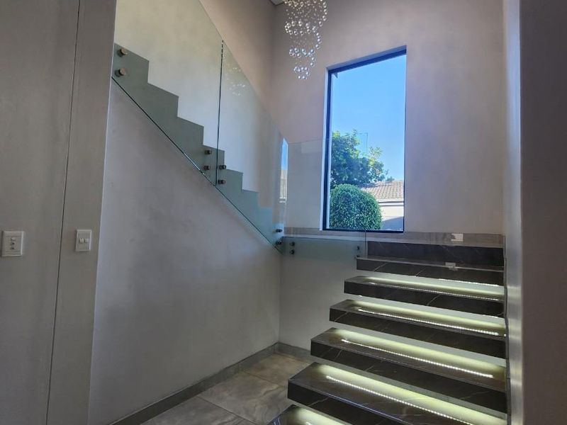 Modern entrance foyer featuring a striking stone staircase with integrated LED lighting, glass balustrade, and a contemporary feature chandelier.