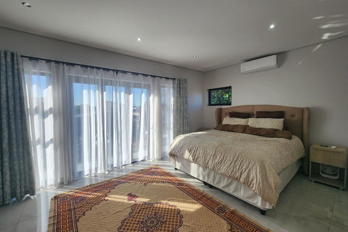 Spacious bedroom featuring tiled flooring, recessed downlighting, a wall-mounted air conditioning unit, and large sliding glass doors providing ample natural light.