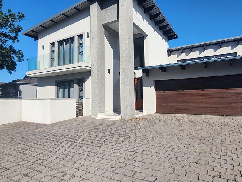 Modern double-story residence featuring a paved driveway, integrated double garage with timber door, and a sleek upper-level balcony with glass balustrades.