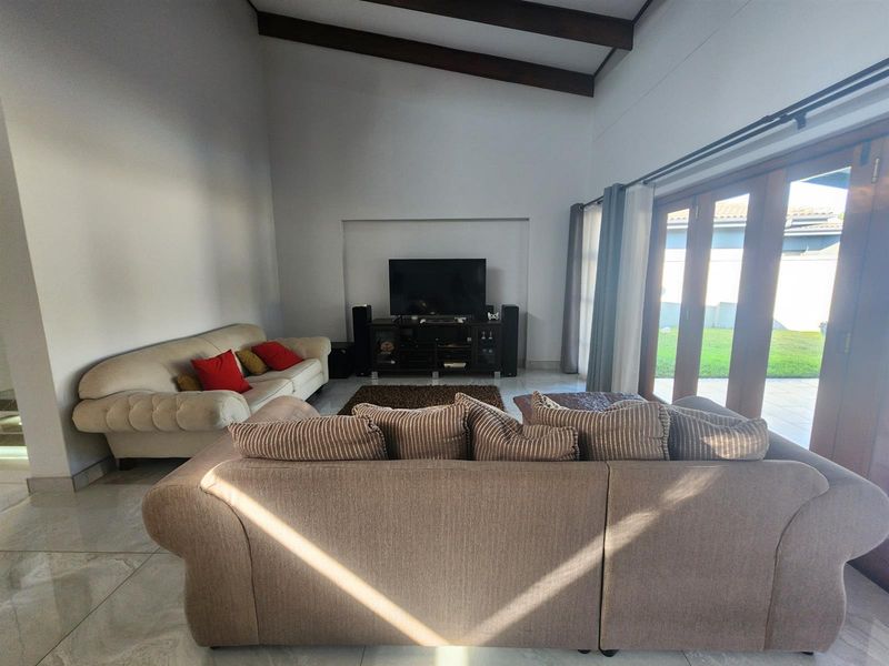 Spacious living room featuring vaulted ceilings with exposed timber beams, tiled flooring, and large timber-framed glass doors opening to the garden.