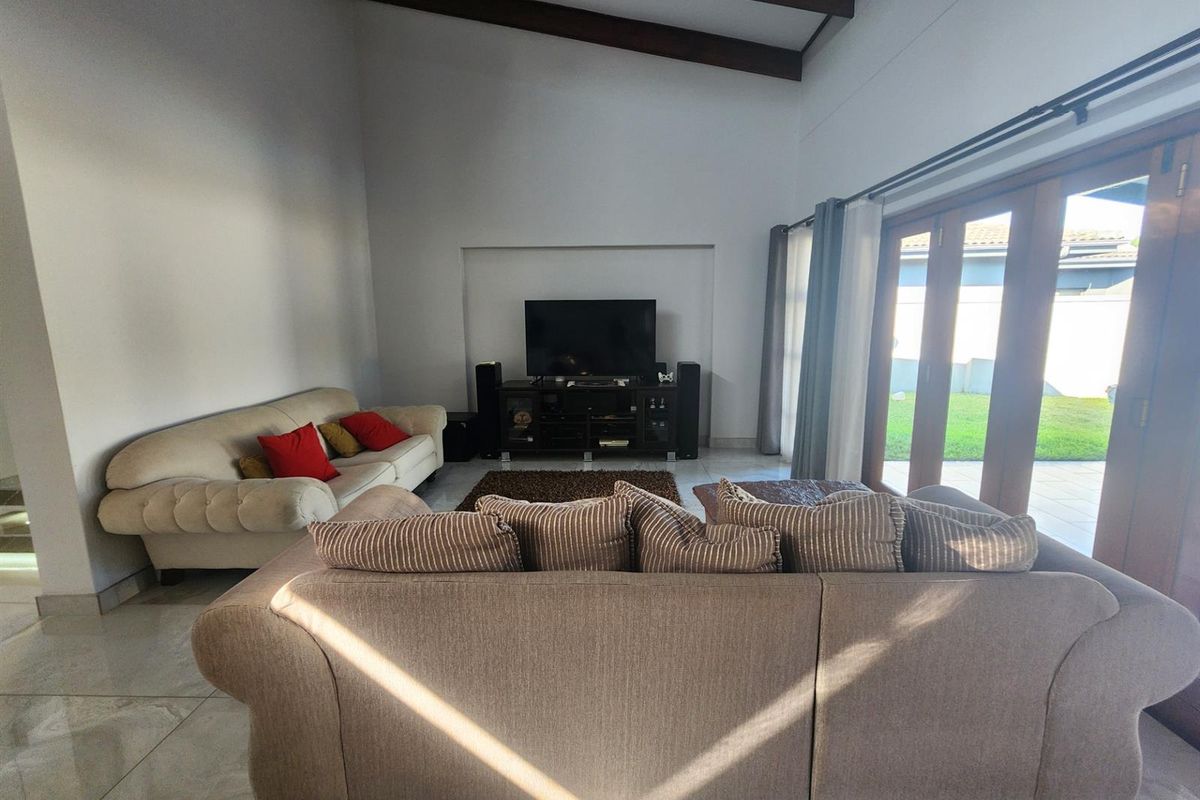 Spacious living room featuring vaulted ceilings with exposed timber beams, tiled flooring, and large timber-framed glass doors opening to the garden.