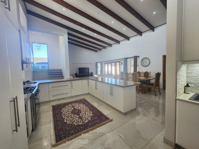 Spacious open-plan kitchen and dining area featuring high vaulted ceilings with exposed timber beams, modern cabinetry, and polished porcelain floor tiles.
