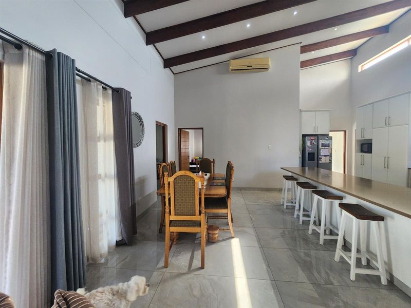 Spacious open-plan living and dining area featuring high vaulted ceilings with exposed timber beams, tiled flooring, and a modern kitchen island with breakfast bar seating.