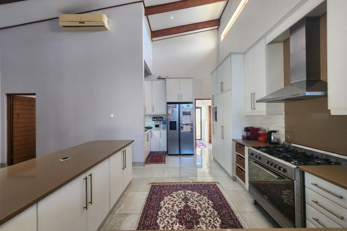 Modern kitchen featuring white cabinetry, stone countertops, gas stove with extractor, and high vaulted ceilings with exposed timber beams.