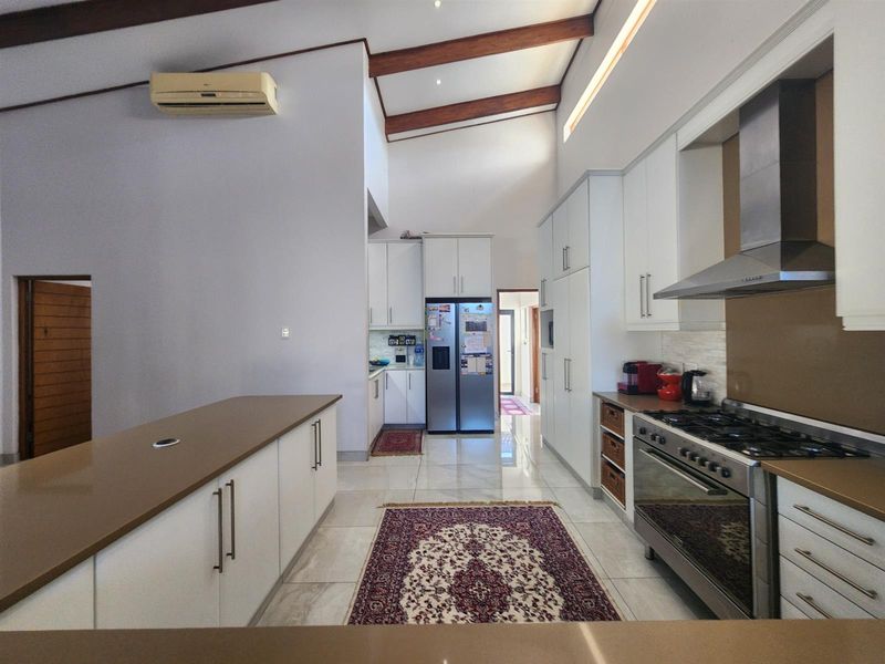 Modern kitchen featuring white cabinetry, stone countertops, gas stove with extractor, and high vaulted ceilings with exposed timber beams.