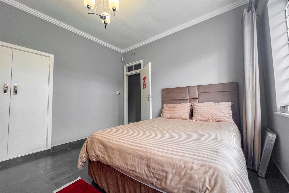 A well-lit bedroom featuring tiled flooring, built-in cupboards, and decorative ceiling cornicing, providing a functional and neutral living space.