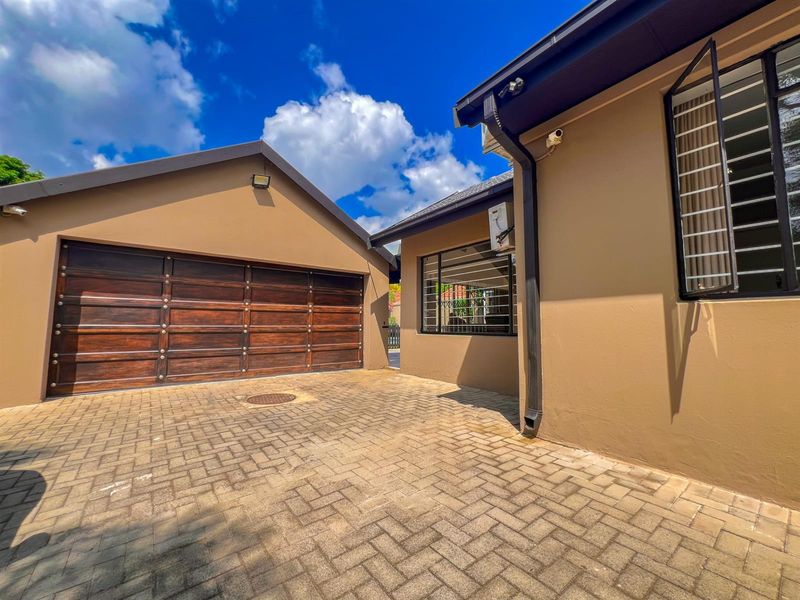 A well-maintained exterior view featuring a paved driveway leading to a wooden sectional garage door and a clean building facade with security bars.