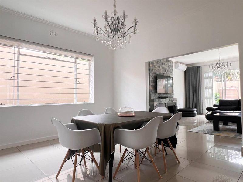 Spacious open-plan dining and living area featuring polished floor tiles, a striking stone feature wall, and elegant crystal chandeliers.