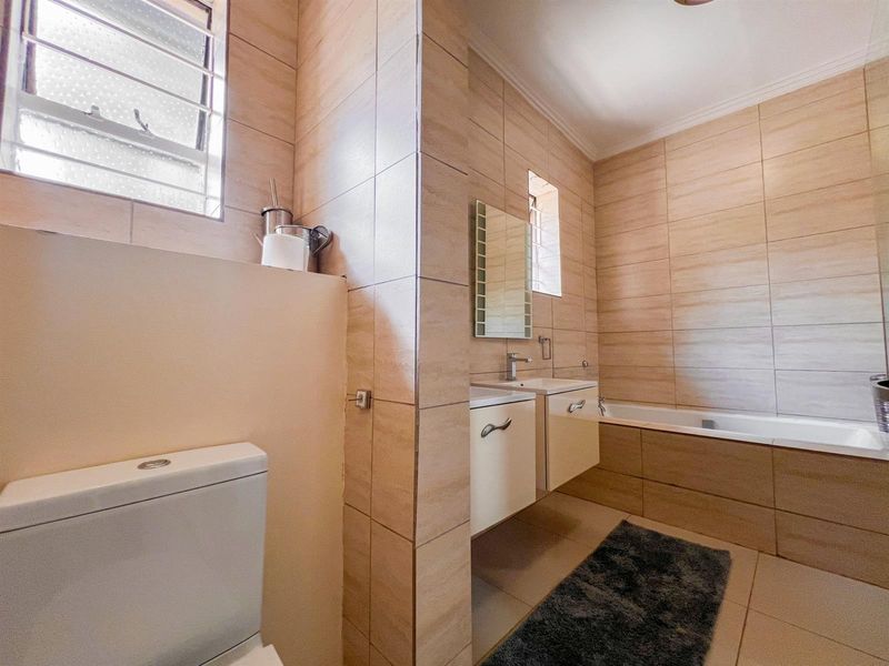 A well-maintained bathroom featuring neutral wall tiles, a built-in vanity with basin, a bathtub, and a separate toilet area.