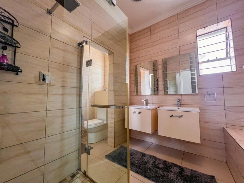 Modern bathroom featuring a double vanity, glass-enclosed shower, and neutral wall tiling, providing a clean and functional space.