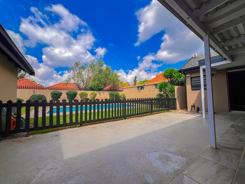 A covered patio area overlooking a private swimming pool and garden, featuring a concrete floor and perimeter wall enclosure.