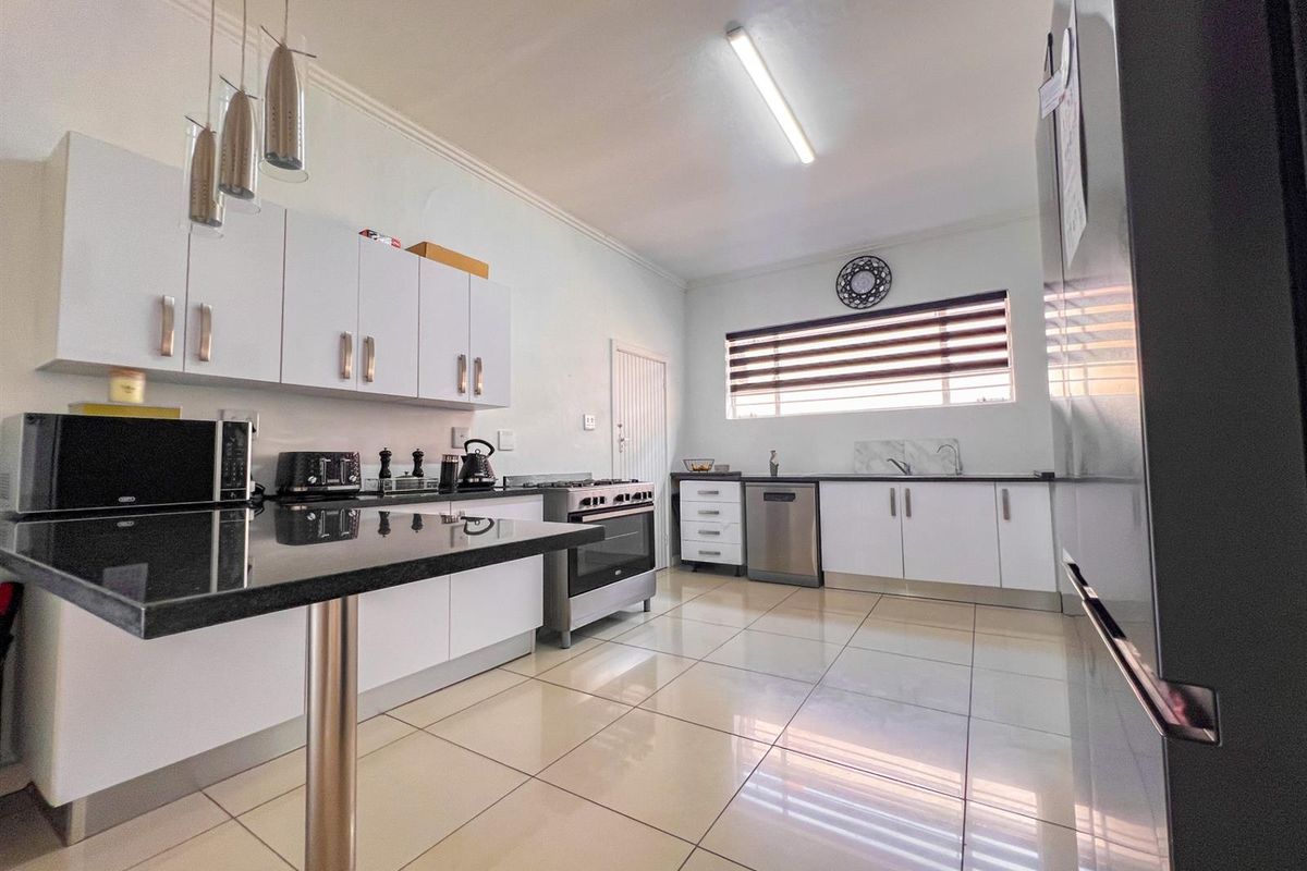 Modern kitchen featuring white cabinetry, black granite countertops, gas stove, and tiled flooring with ample workspace and integrated appliance connections.