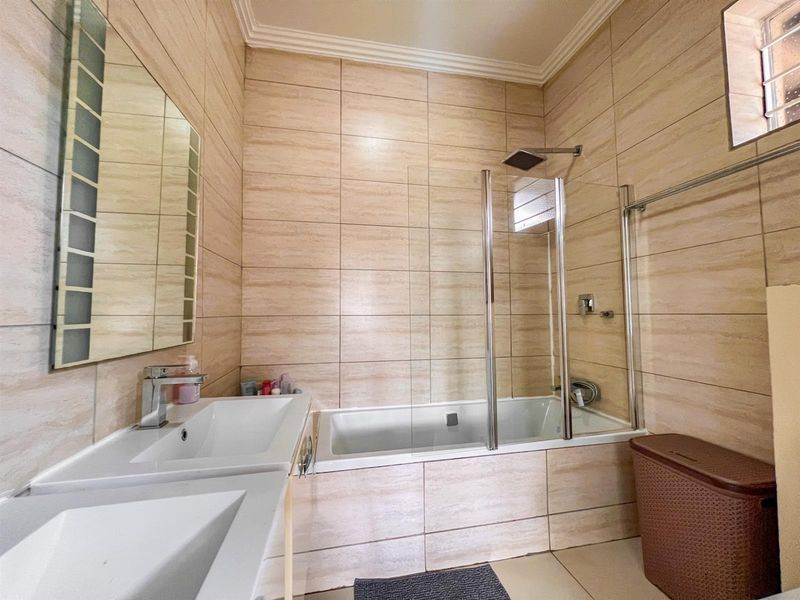 Modern bathroom featuring a double vanity, a built-in bathtub with a glass shower screen, and floor-to-ceiling tiled walls.