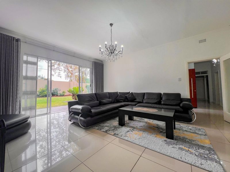 Spacious living room featuring polished porcelain floor tiles, a decorative crystal chandelier, and large sliding glass doors providing direct access to the garden.