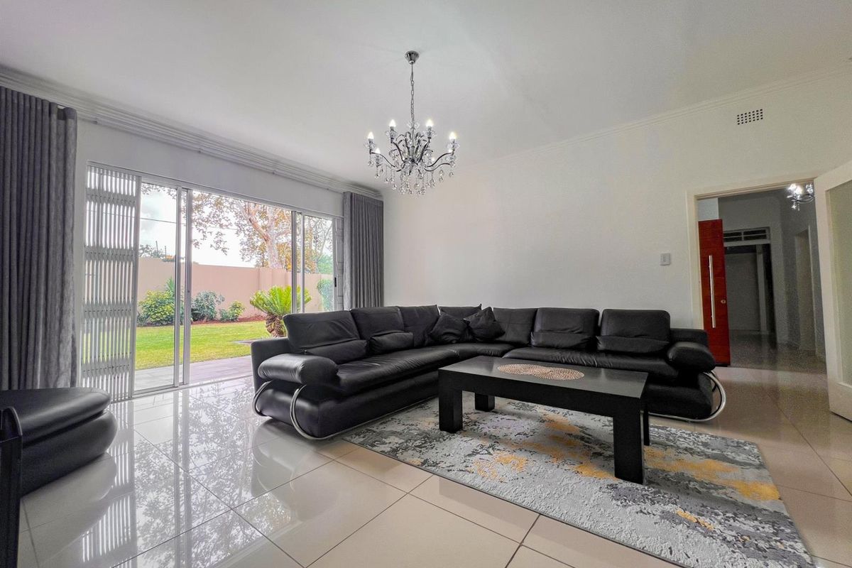 Spacious living room featuring polished porcelain floor tiles, a decorative crystal chandelier, and large sliding glass doors providing direct access to the garden.