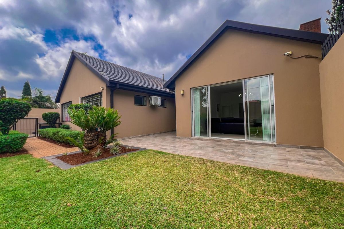 Rear view of the property featuring a tiled patio, well-maintained lawn, and sliding glass doors providing access to the interior living space.