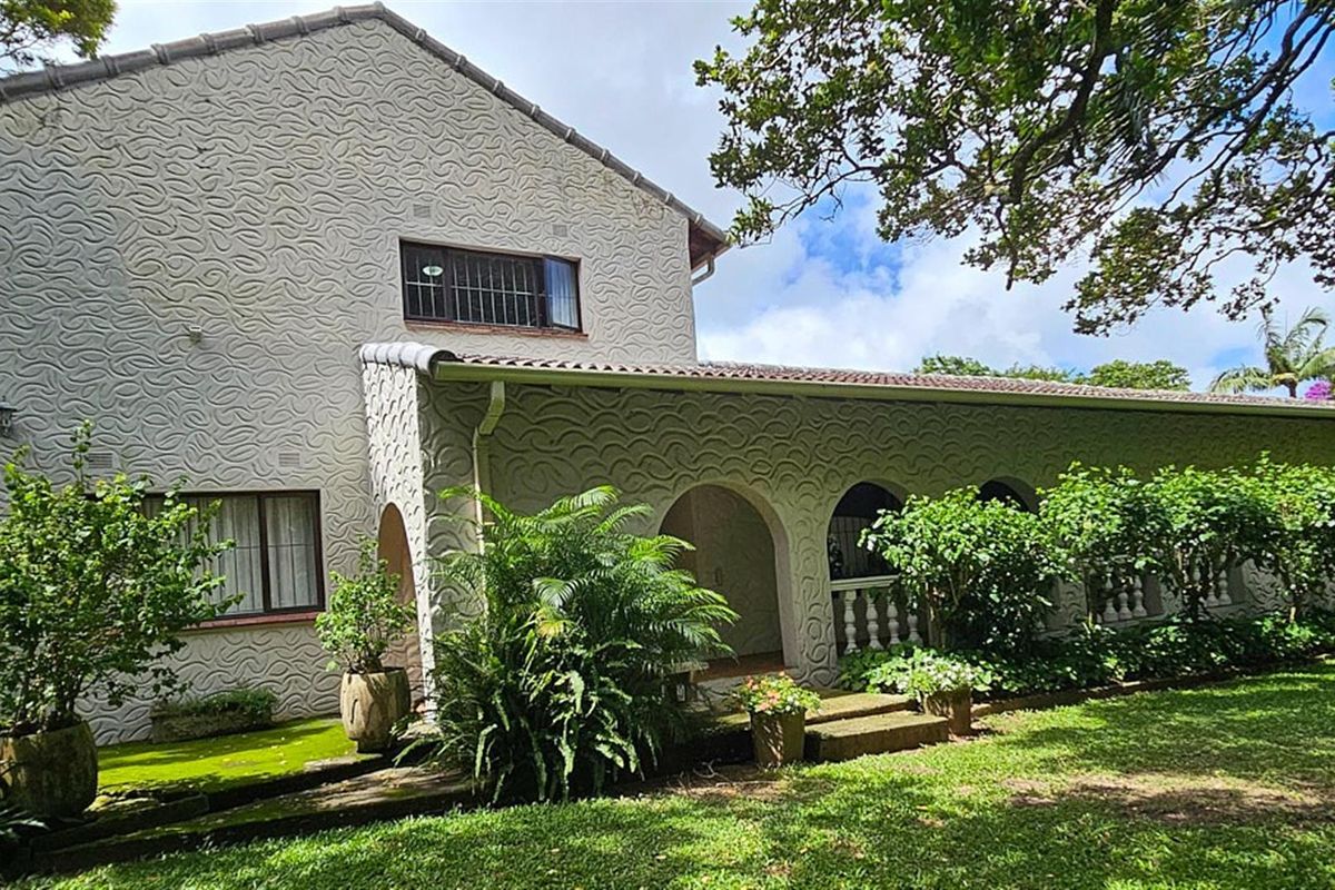 A view of the rear exterior of the house featuring a covered patio with arched openings and a textured facade set within a garden.