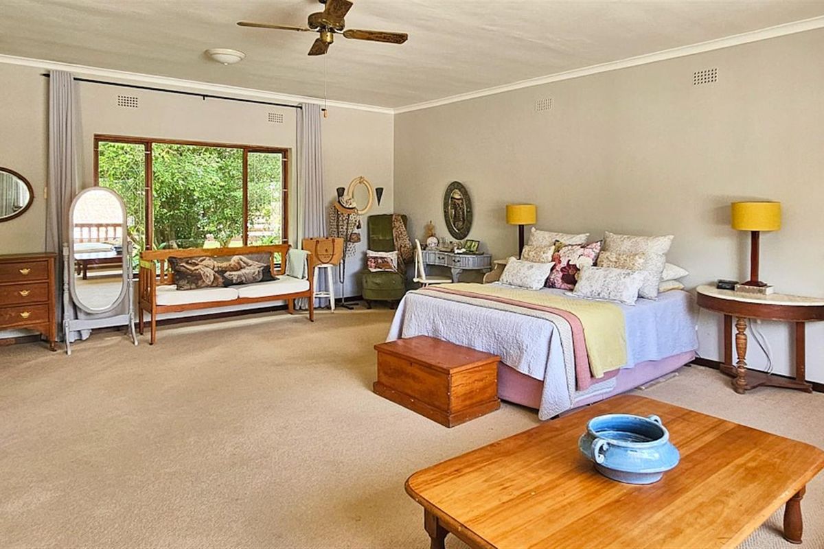 Spacious bedroom featuring large windows with garden views, neutral wall finishes, and a ceiling fan.