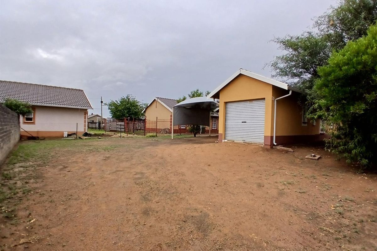 A view of the rear yard featuring a detached garage with a roller door and a shade-cloth carport structure.