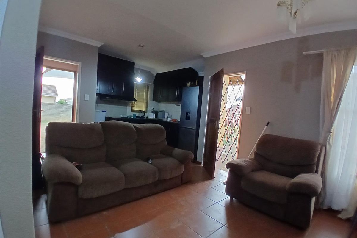 Open plan living area featuring tiled flooring, direct access to outdoor spaces, and a compact kitchen with dark cabinetry.