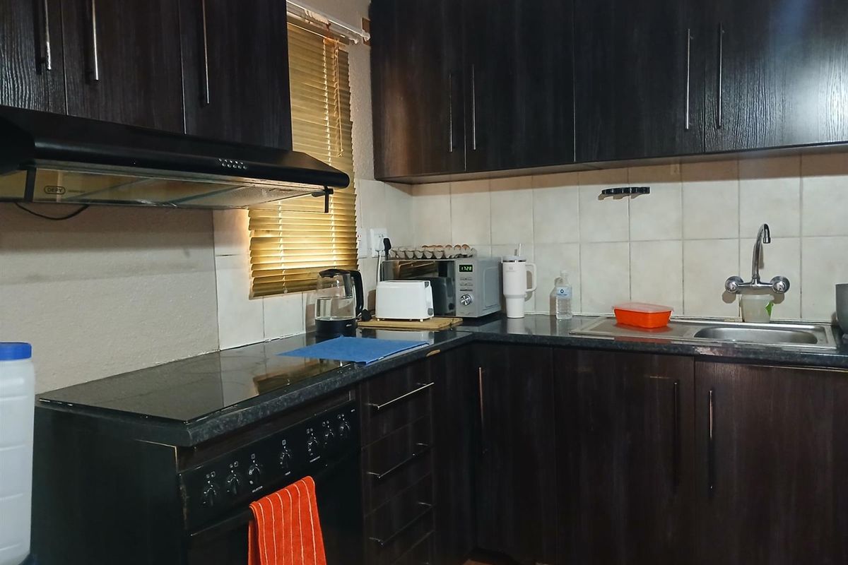 A functional kitchen featuring dark wood cabinetry, a built-in stove with extractor fan, tiled backsplash, and a stainless steel sink.