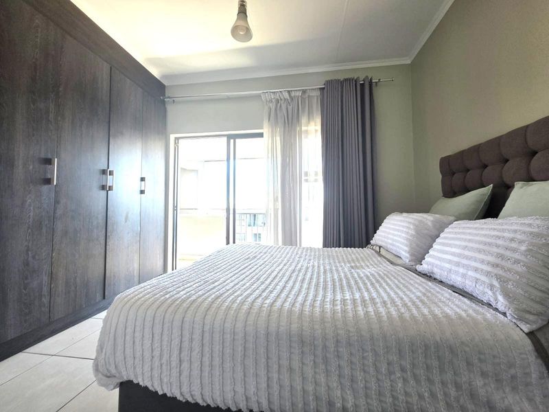 A well-maintained bedroom featuring dark wood built-in cupboards, tiled flooring, and a sliding glass door providing access to an outdoor area.