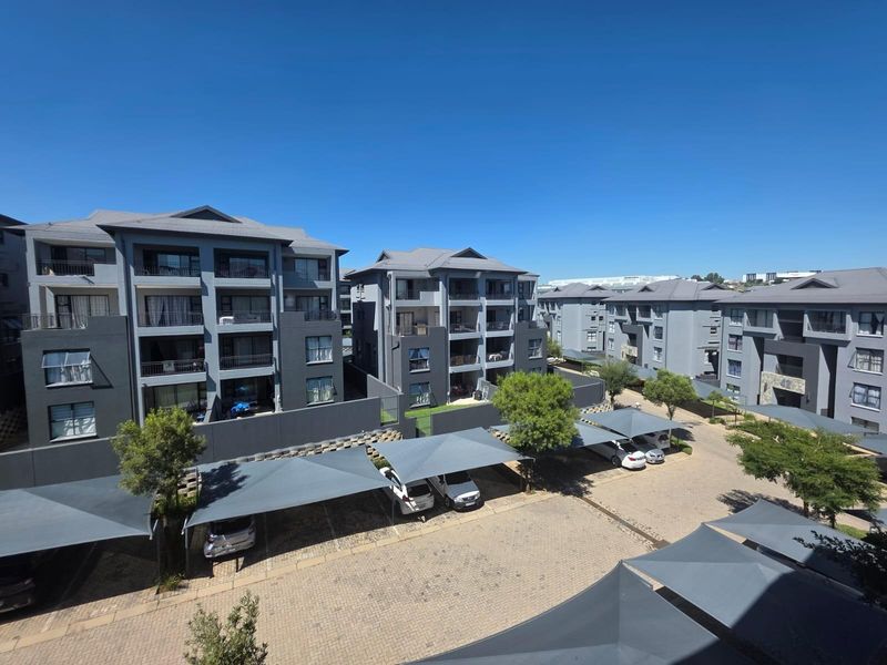 An elevated view of a modern apartment complex featuring multi-story buildings, paved driveways, and covered parking structures.