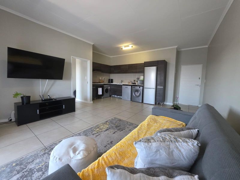 An open-plan living area featuring a modern kitchen with dark cabinetry, tiled floors, and a functional layout connecting to the lounge space.
