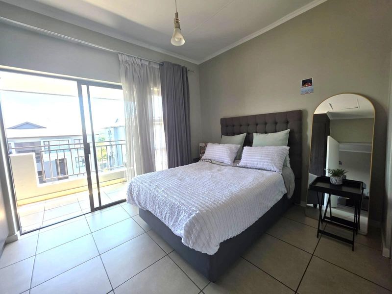 A well-lit bedroom featuring tiled flooring and a large sliding glass door providing direct access to a private balcony.