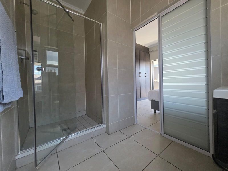 Modern bathroom featuring a glass-enclosed shower, neutral wall and floor tiling, and a sliding door providing access to the adjacent bedroom.