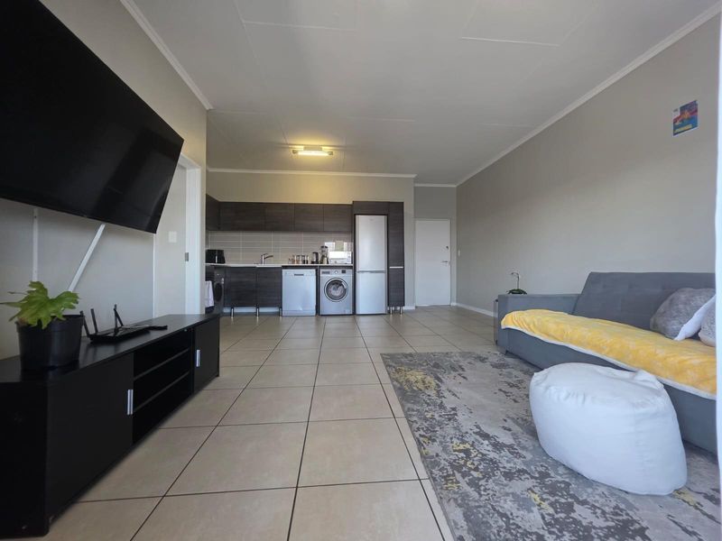 Open-plan living area featuring tiled flooring and a functional kitchen with built-in cabinetry, seamlessly connecting the lounge and kitchen spaces.