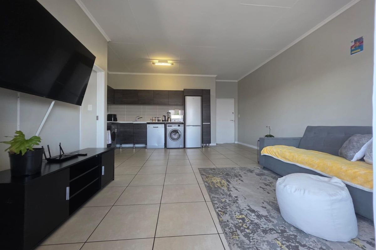 Open-plan living area featuring tiled flooring and a functional kitchen with built-in cabinetry, seamlessly connecting the lounge and kitchen spaces.