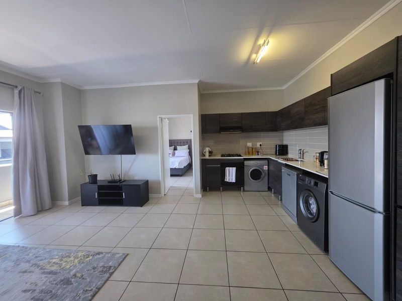 Open-plan living area featuring a modern kitchen with dark cabinetry, tiled flooring, and seamless flow to the adjacent bedroom.