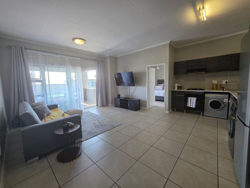 Open-plan living area featuring tiled floors, a modern kitchen with built-in appliances, and direct access to a private balcony through sliding glass doors.