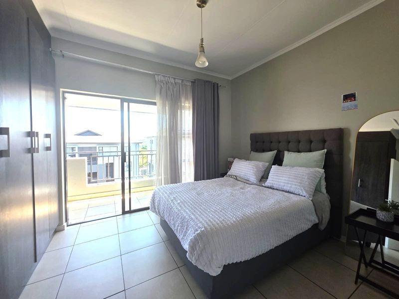 A well-lit bedroom featuring tiled flooring, built-in cupboards, and a sliding glass door providing direct access to a private balcony.