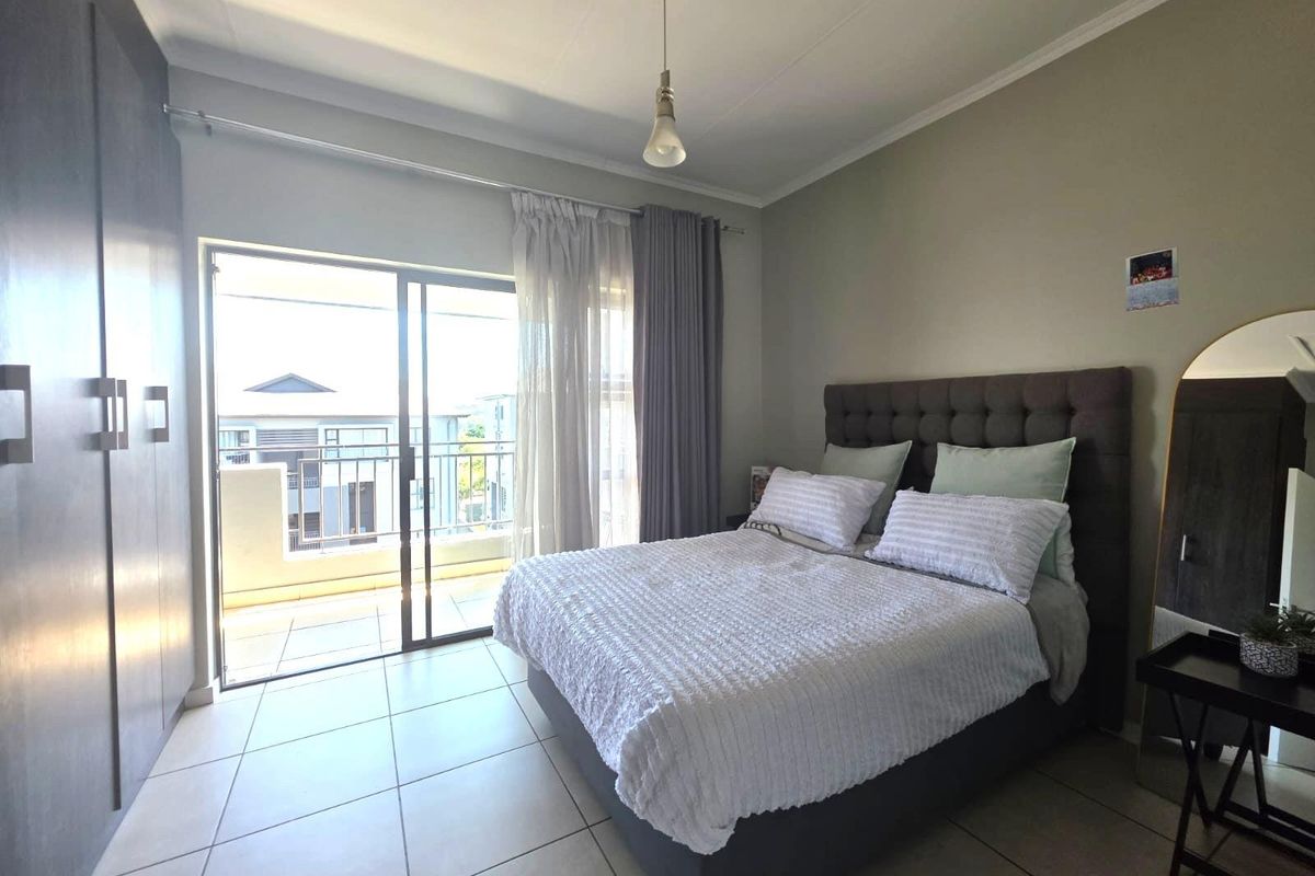 A well-lit bedroom featuring tiled flooring, built-in cupboards, and a sliding glass door providing direct access to a private balcony.