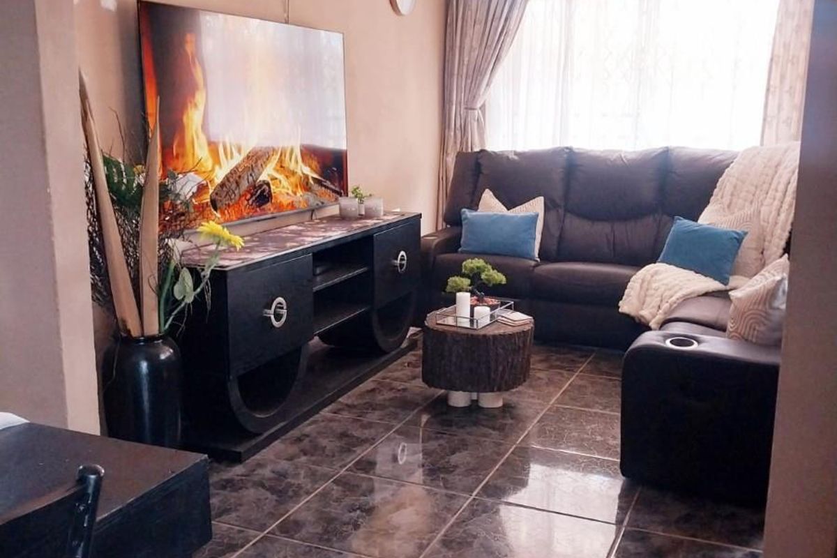 A cozy living room featuring dark marble-effect floor tiles, neutral wall tones, and large windows allowing for natural light.