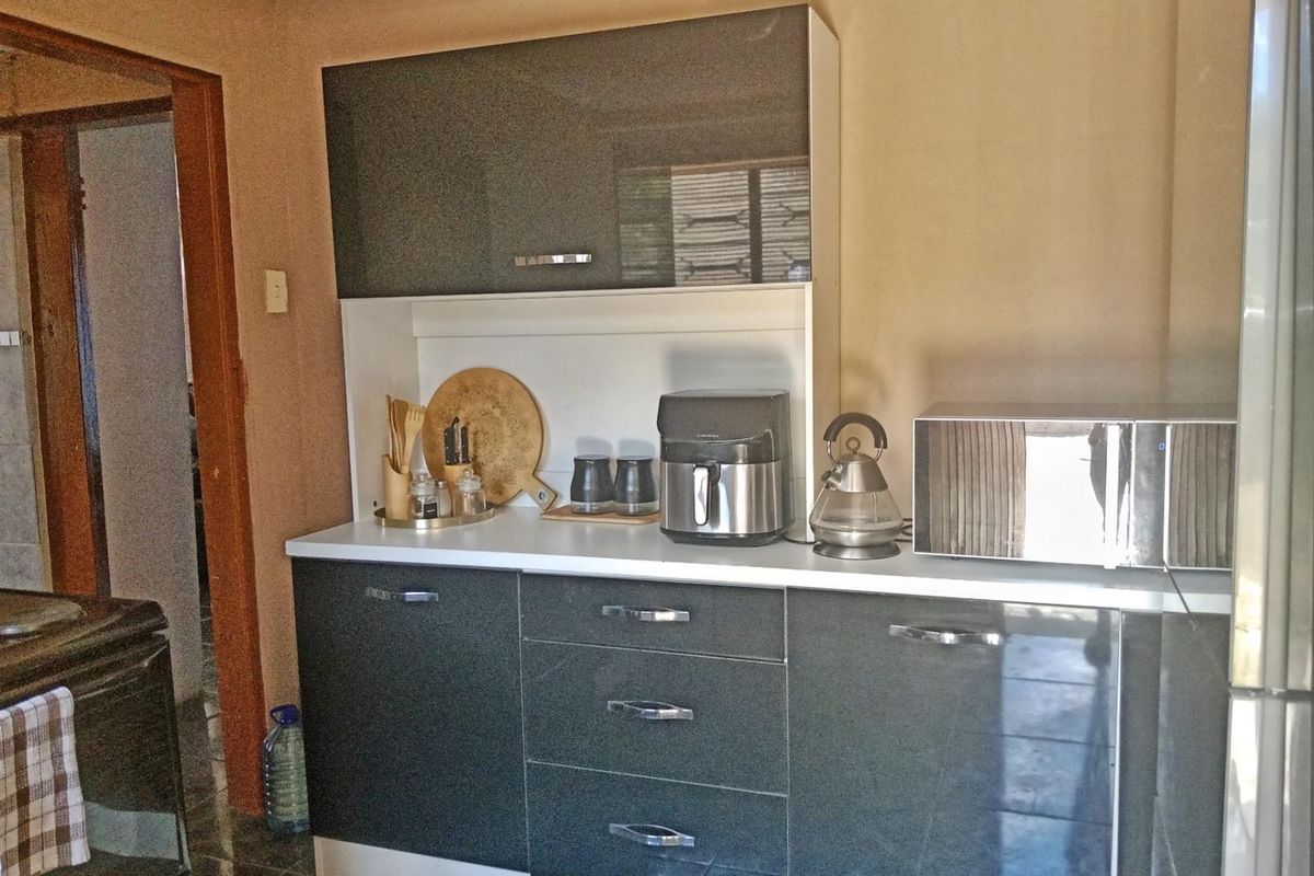 A compact kitchen area featuring modern dark grey high-gloss cabinetry, white countertops, and integrated storage space.