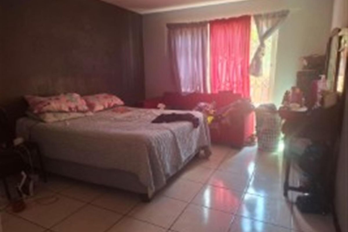 A bedroom featuring tiled flooring and a large window with curtains, providing natural light to the space.